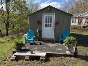 Een klein tuinhuisje met een witte deur, twee blauwe stoelen en een bloempot.