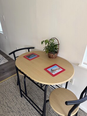 Een ronde tafel met twee stoelen, een kleine potplant en twee rode placematen met afbeeldingen.