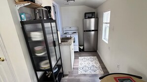 Cocina con refrigerador, estufa, microondas y una alacena negra con vajilla.