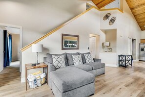 Ein modernes Wohnzimmer mit einem grauen Ecksofa, Holzboden, Holzzieldecke und einer Treppe.