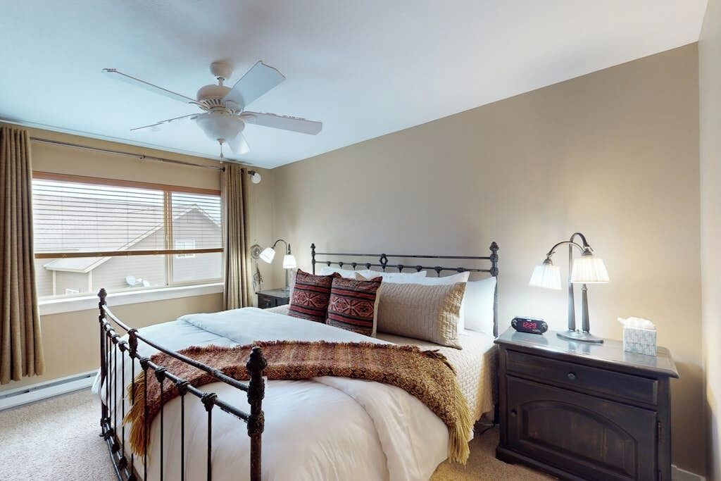 A bedroom with a bed, a nightstand, a ceiling fan, and a window with curtains.