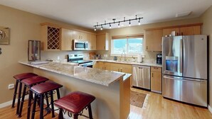 A modern kitchen with a large island, stainless steel appliances, and wooden cabinets. - Modern Mountain Getaway with New Hot Tub – Big Sky, Montana (Big Sky)