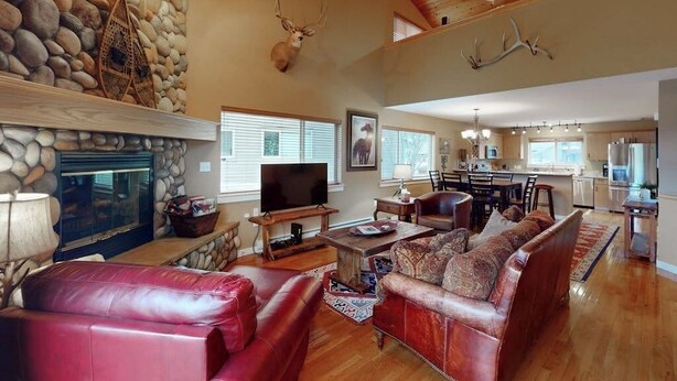 A spacious living area with a fireplace, leather sofas, a television, and a stone wall. - Modern Mountain Getaway with New Hot Tub – Big Sky, Montana (Big Sky)