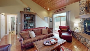 A living room with a wooden ceiling, a fireplace, a red leather sofa, a red armchair, and a bookshelf. - Modern Mountain Getaway with New Hot Tub – Big Sky, Montana (Big Sky)