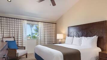 A hotel room with a bed, a desk, a chair, a window with curtains, and a ceiling fan.