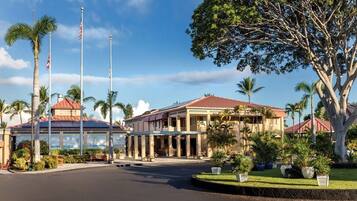 A hotel with a large building, palm trees, and a flagpole.