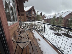 Eine Holzterrasse mit Stühlen, verschneiter Erde und Blick auf Holzhäuser.