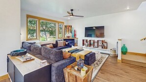 Een moderne woonkamer met een hoekbank, een flatscreen televisie en een plafondventilator.