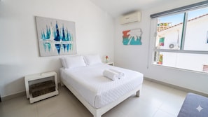 Ein Schlafzimmer mit Bett, Nachttisch, Wand-Klimaanlage und Fenster mit Außenblick.