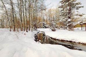 A snow-covered landscape with a bridge over a stream, trees, and a building in the background. - Lovely home with well-equipped kitchen & back deck - walk to shopping & dining (Wilson)
