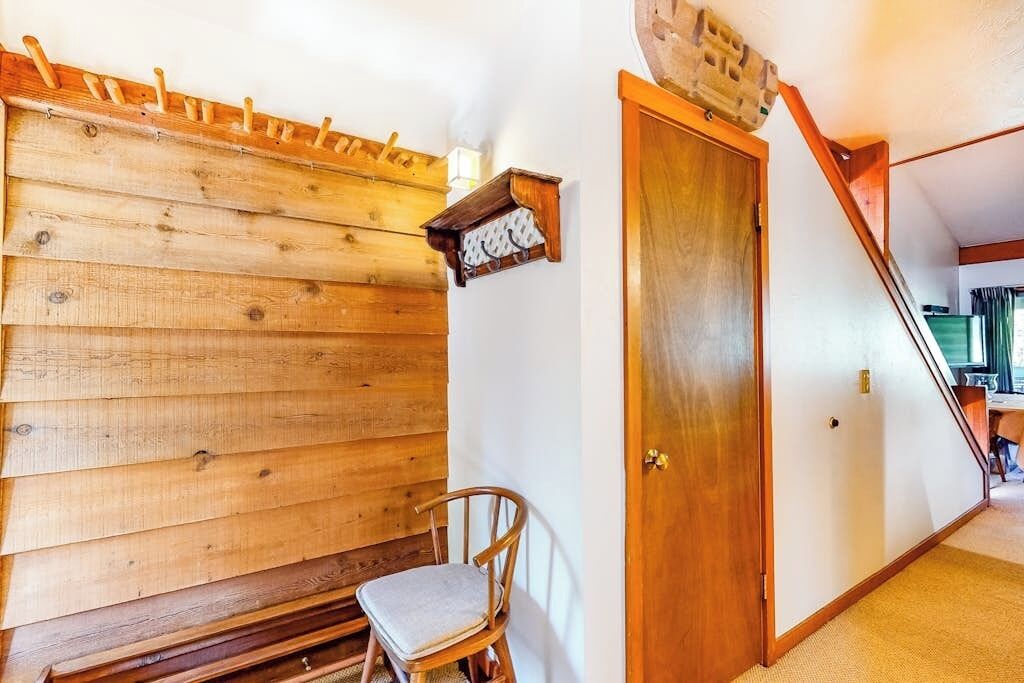 Pared de madera con un banco, una silla y una puerta con lámpara.
