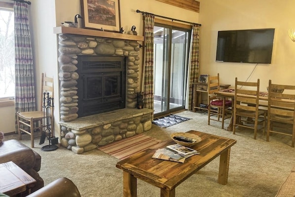 Ein Wohnzimmer mit Kamin aus Stein, einem an der Wand montierten Fernseher und einem Essbereich mit Holztisch und -stühlen.