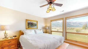 A bedroom with a bed, bedside tables, a ceiling fan, and large windows with a mountain view. - Beautiful family home w/full kitchen and gorgeous views from living room (Wilson)