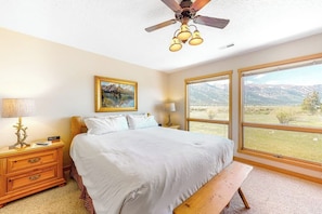 A bedroom with a bed, bedside tables, a ceiling fan, and large windows with a mountain view. - Beautiful family home w/full kitchen and gorgeous views from living room (Wilson)