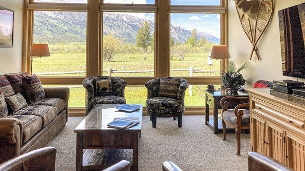 A living room with a large window, leather furniture, a coffee table, and a mounted animal head. - Beautiful family home w/full kitchen and gorgeous views from living room (Wilson)