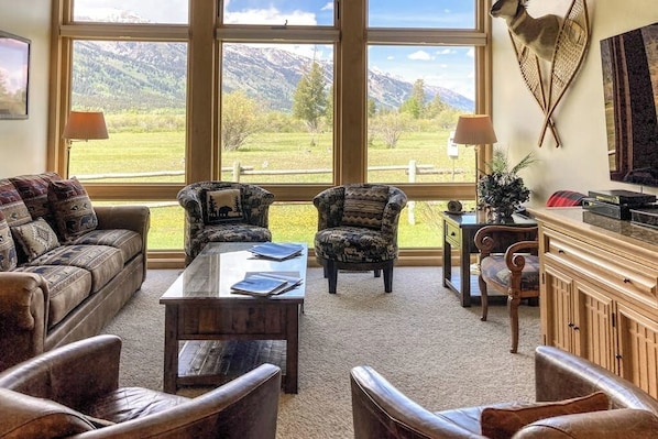 A living room with a large window, leather furniture, a coffee table, and a mounted animal head. - Beautiful family home w/full kitchen and gorgeous views from living room (Wilson)