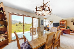 A dining area with a glass table, wooden chairs, a chandelier, and a view of mountains through large sliding doors. - Beautiful family home w/full kitchen and gorgeous views from living room (Wilson)