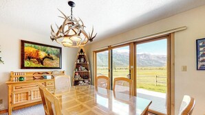 A dining area with a glass table, chairs, a wooden buffet, a chandelier, and a large window with a mountain view. - Beautiful family home w/full kitchen and gorgeous views from living room (Wilson)