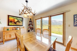 A dining area with a glass table, chairs, a wooden buffet, a chandelier, and a large window with a mountain view. - Beautiful family home w/full kitchen and gorgeous views from living room (Wilson)