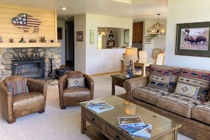 A living room with leather armchairs, a sofa with patterned cushions, a glass coffee table, a fireplace, and a buffalo-themed wall decoration. - Beautiful family home w/full kitchen and gorgeous views from living room (Wilson)