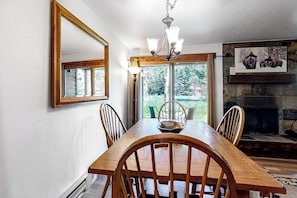 Ein Esszimmer mit Holztisch, Stühlen, einer Chandelierleuchtre, einem Kamin und einem großen Fenster.