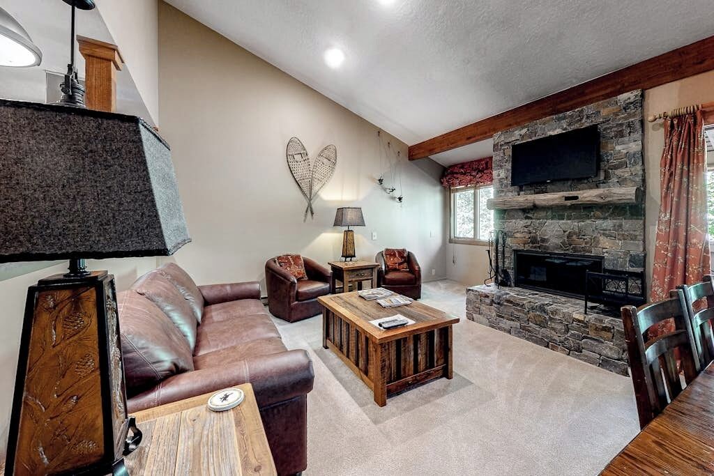 A living room with a stone fireplace, leather sofa, wooden coffee table, and a flat-screen TV mounted on the wall.