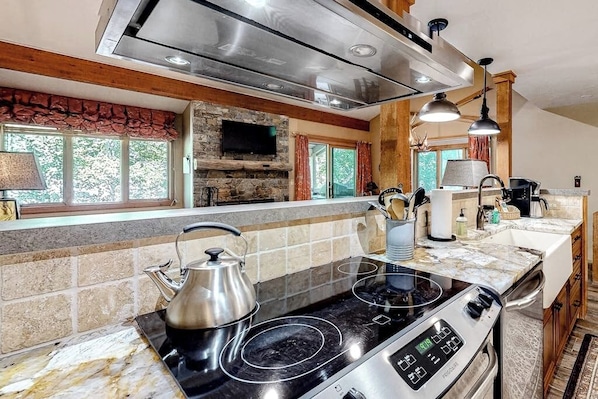 A kitchen with a stone fireplace, a stove, and a large window. - Beautiful condo with full kitchen, mountain views (Wilson)