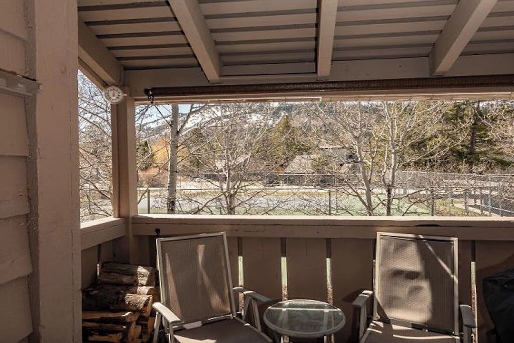 A covered porch with a view of trees and a fence.