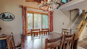 Un comedor con una mesa y sillas de madera, una araña y una escalera.