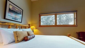 A neatly made bed with white linens and a headboard, a window with a view of snow-covered trees, and a framed picture on the wall. - Beautiful country home with full kitchen & views from the private balcony (Wilson)