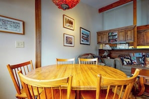 A wooden dining table surrounded by chairs, a bookshelf, and a sofa in a room with wooden beams and framed pictures on the wall. - Beautiful country home with full kitchen & views from the private balcony (Wilson)