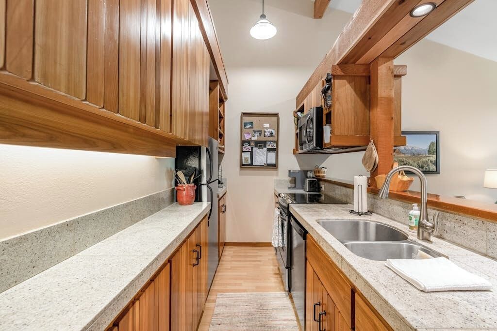 A kitchen with wooden cabinets, granite countertops, a stainless steel sink, and a microwave.