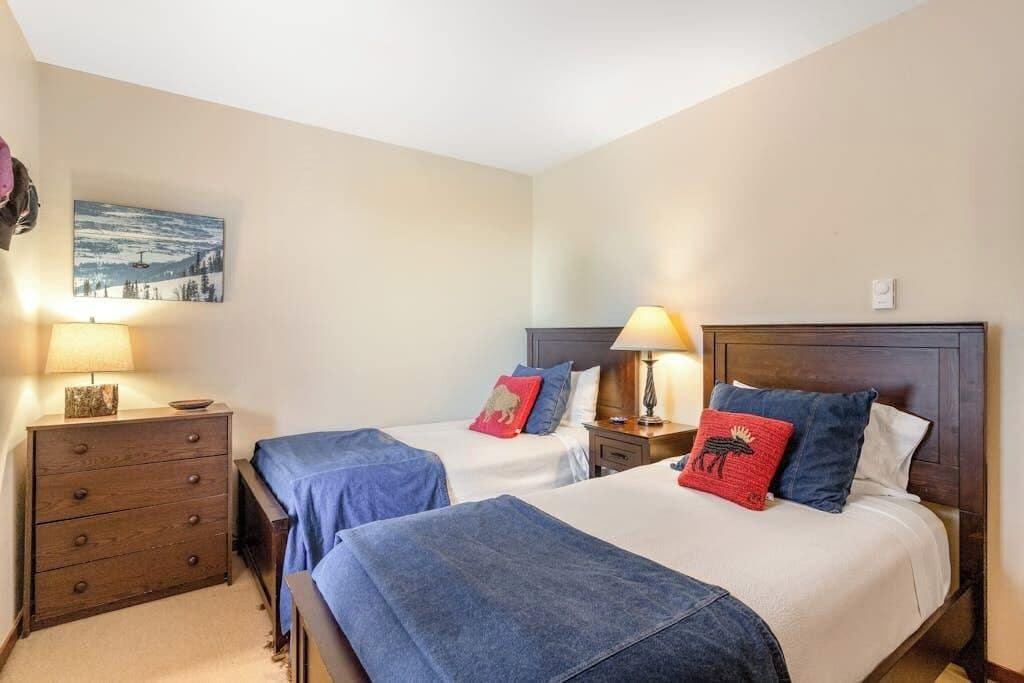 A hotel room with two beds, a dresser, a nightstand, and a painting on the wall.