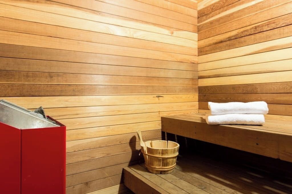 Un sauna avec des murs en bois, un banc, un appareil de chauffage rouge et un seau en bois.