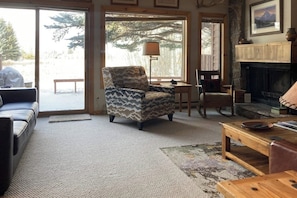 A cozy living room with a patterned armchair, a fireplace, and a view through a large window. - Amazing country getaway with deck & mountain views (Jackson)