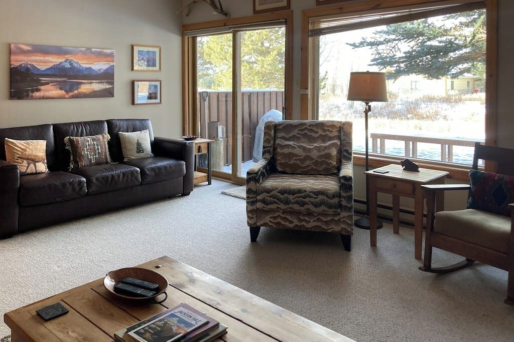 A living room with a sofa, armchair, coffee table, and a view through a sliding door.