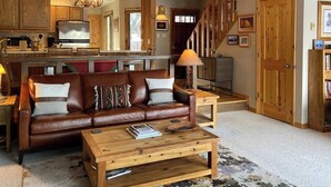 Ein geräumiger Wohnbereich mit einem braunen Ledersofa, einem Holztisch und einem Fernseher im Hintergrund.