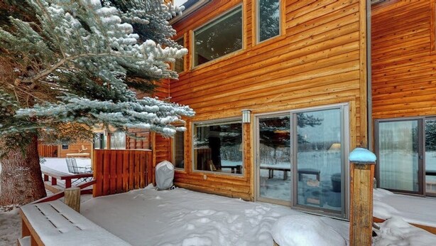 Eine Holzhütte mit überdachter Veranda, einer Bank und einem mit Schnee bedeckten Baum.