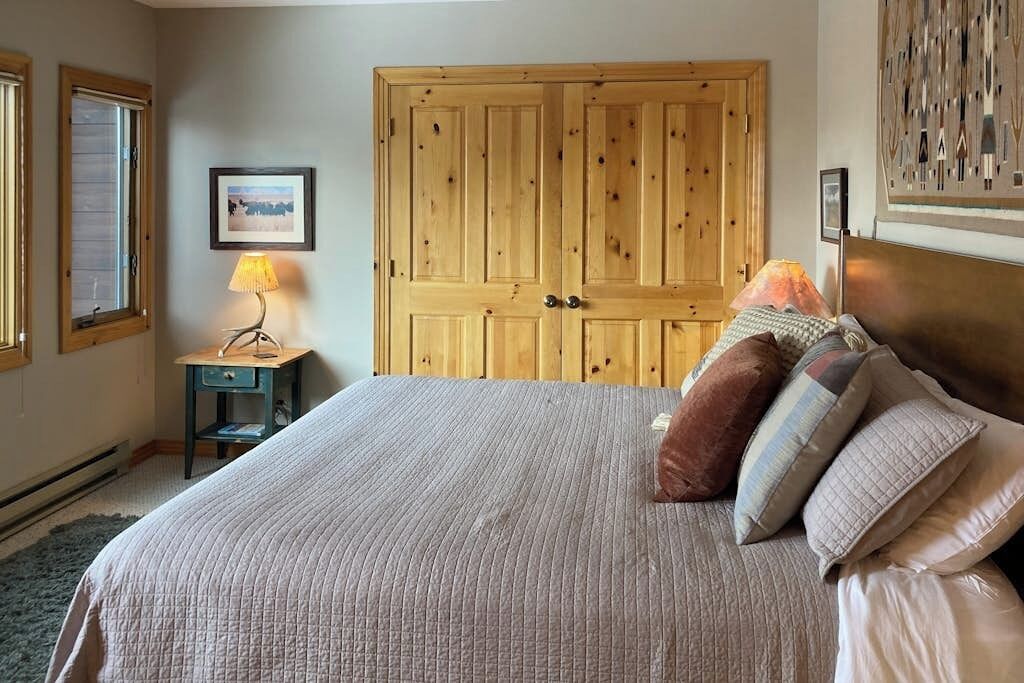 Un dormitorio con una cama grande, un armario de madera, una mesita con una lámpara y un cuadro enmarcado en la pared.