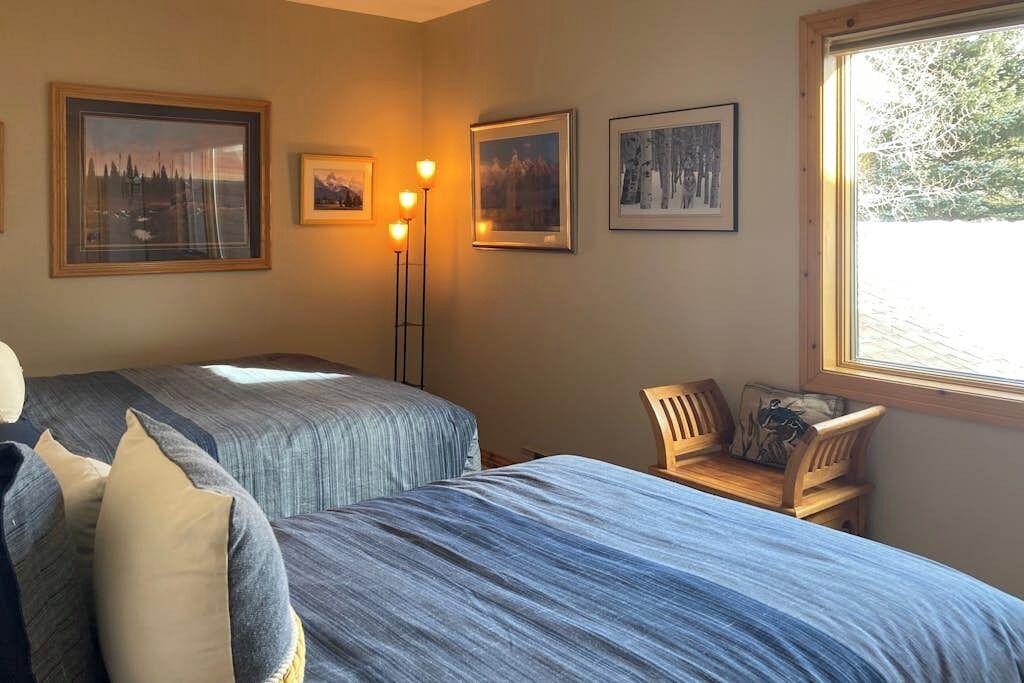 A room with two beds, a chair, and framed pictures on the wall.