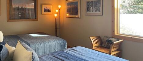 A room with two beds, a chair, and framed pictures on the wall.