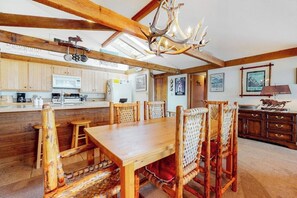 Une cuisine rustique avec des poutres en bois, un lustre et un coin repas comprenant une table en bois et des chaises en osier.