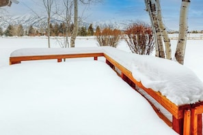 Un banc en bois recouvert de neige, entouré d’arbres et dominant un paysage enneigé.