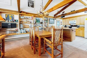 A rustic dining area with a wooden table and chairs, a chandelier, and a kitchen with wooden cabinets and a microwave. - Country townhome next to golf course with mountain view & vaulted ceilings (Jackson)