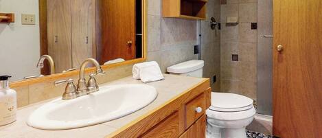 A bathroom with a wooden vanity, a sink, a toilet, and a shower area.