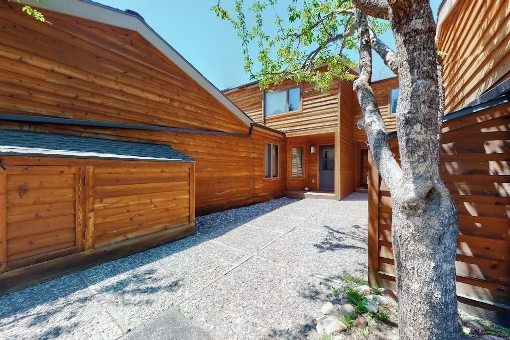 A wooden cabin with a gravel driveway, a wooden fence, and a tree.