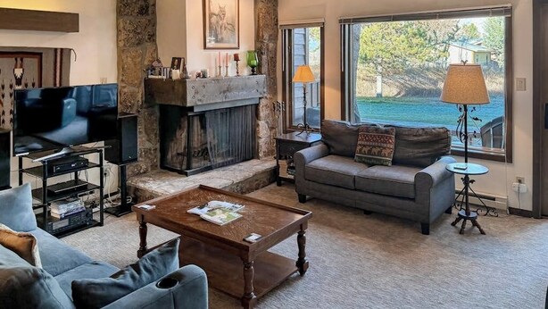 A living room with a fireplace, a sofa, a coffee table, and a TV. - Rustic townhome near golf course with private sauna & deck (Jackson)