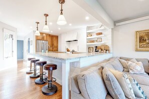 A modern kitchen with a central island, bar stools, and a seating area with a sofa.