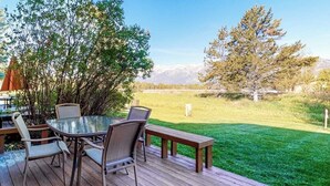 Una terraza con una mesa y sillas de vidrio, rodeada de césped y árboles.