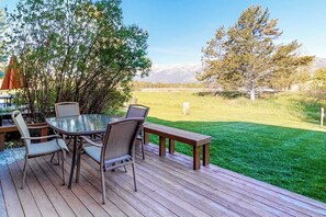 Eine Terrasse mit Tisch und Stühlen mit Glasplatte, umgeben von einer Rasenfläche und Bäumen.